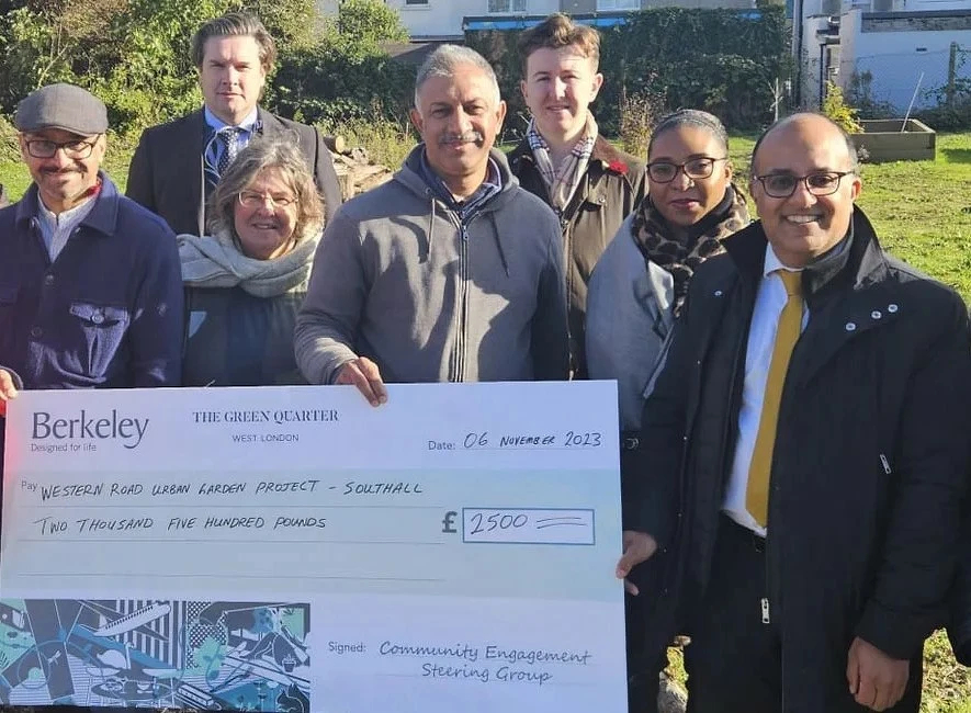 A group of people is holding a large ceremonial check for £2,500 from Berkeley for the Western Road Urban Garden Project in Southall. Jags Sanghera is on the right.