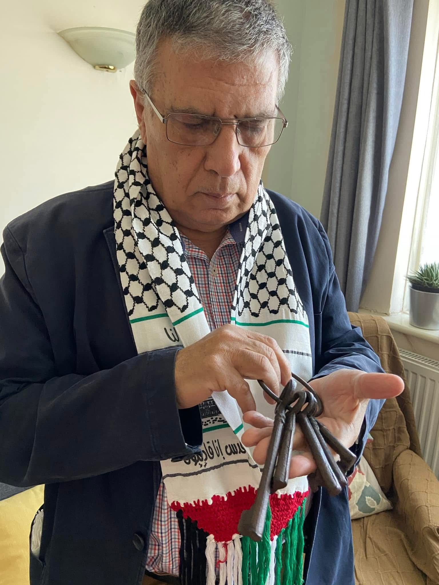 Yousef Qandeel wearing glasses and a Palestinian scarf (keffiyeh) is holding a bunch of old keys.
