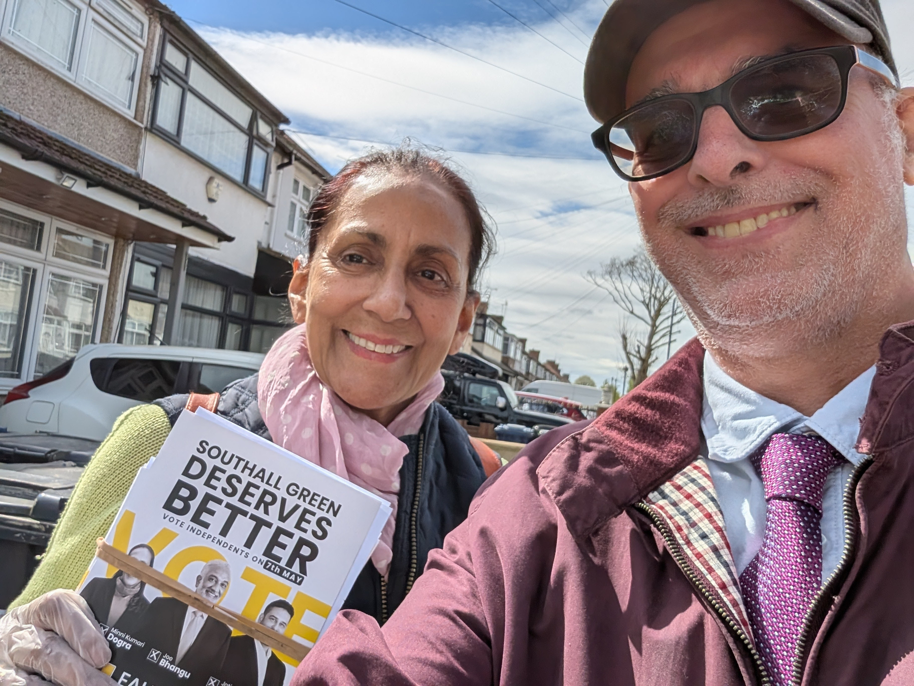 Ealing Community Independents councillor candidate, Minni Dogra, and supporter and Southall Stories writer David Marsden are smiling at the camera, holding a flyer related to Southall Green.